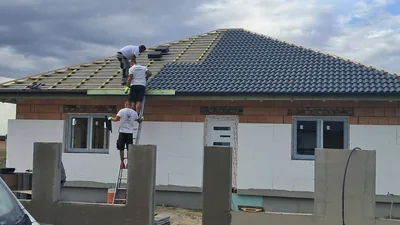 Érd – Tetőfedők sötétszürke cserepeket raknak a családi ház tetősíkjára.