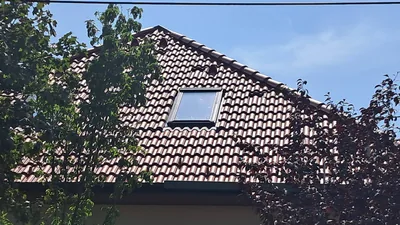 Százhalombatta – A kész cseréptető egy tetőablakkal, a kert fái közül nézve.